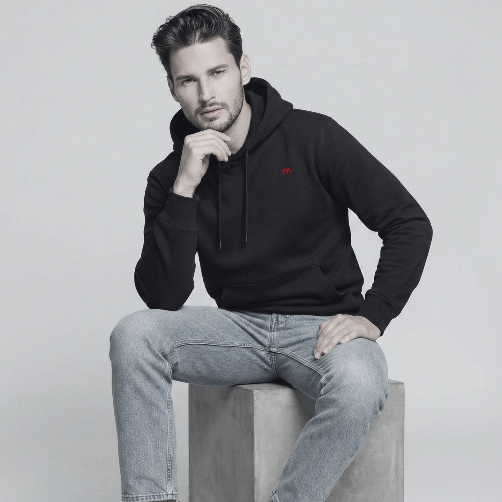 Male model wearing the Rascal Nation black hoodie with red rn. logo, styled with jeans and boots in a minimal studio.